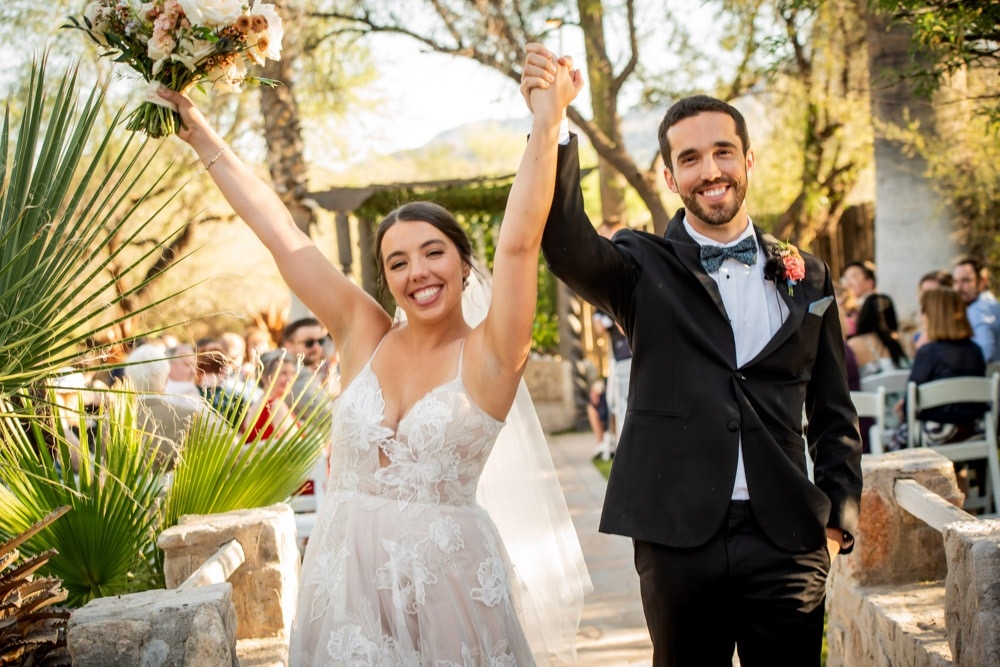 Bride and groom joining hands in a cheer as they make their way back up the aisle